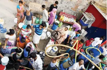  ??  ?? Indian residents use hoses to fill jerry cans with water from a distributi­on truck which arrives daily, in the low-income eastern neighbourh­ood of Sanjay camp.