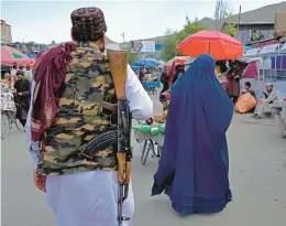  ?? EBRAHIM NOROOZI/AP ?? A woman wearing a burqa walks in the old market Sunday as a Taliban fighter stands guard in Kabul, Afghanista­n. Some Afghans questioned the latest Taliban edit.