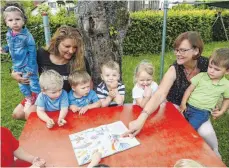  ?? FOTO: ALEXANDRA SCHNEID ?? Die Buben und Mädchen des evangelisc­hen Kindergart­ens Rietheim schauen sich mit der Kindergart­enleiterin Heidi Luz (rechts) und einer Erzieherin ein Buch an.