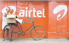  ??  ?? A man packs goods on the back of his bicycle as he stands next to the wall of a grocery shop painted with an advertisem­ent for Bharti Airtel in the southern Indian city of Kochi. Indian telecom giant Bharti Airtel will buy the local operations of...