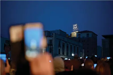  ?? Staff photo by Hunt Mercier ?? ■ Attendees of the Hotel Grim lighting ceremony hold their phones out to record and photograph the lighting of the sign for the first time in 30 years on Tuesday outside the Perot Theatre in Texarkana, Texas.