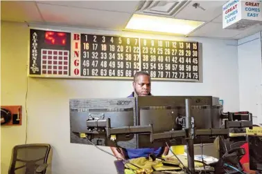  ?? STAFF PHOTOS BY TIM BARBER ?? Avenger Logistics freight broker Chris Mayes stands at his desk in front of a Bingo board where employee achievemen­ts are displayed.