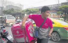  ??  ?? ABOVE A Foodpanda driver talks on his smartphone while zipping up an insulated food bag on a motorcycle in Bangkok.
