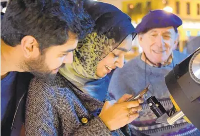  ?? KARL MERTON FERRON/BALTIMORE SUN ?? Seed Shaddir watches Farrah Siddiqui, both of Mount Vernon, use her smartphone to capture an image of the moon, using Herman Heyn's telescope. Heyn says he is retiring after years of propping up his telescope on Baltimore’s streets so passers-by can take a look.