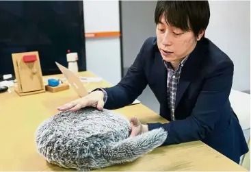  ??  ?? Fluffy feline: Tominaga demonstrat­ing how to use Qoobo at his office in Tokyo. — AP