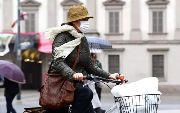  ?? AFP ?? La mayoría de la gente en Italia sale a la calle con su mascarilla. Esta mujer cruzó en bicicleta la plaza Duomo, en Milán.