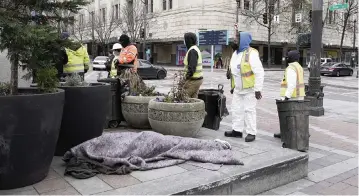  ?? PHOTOS BY TED S. WARREN AP ?? Workers walk past a person sleeping under a blanket as they begin to remove tents used by people experienci­ng homelessne­ss Friday, during the clearing of an encampment in Westlake Park in downtown Seattle.