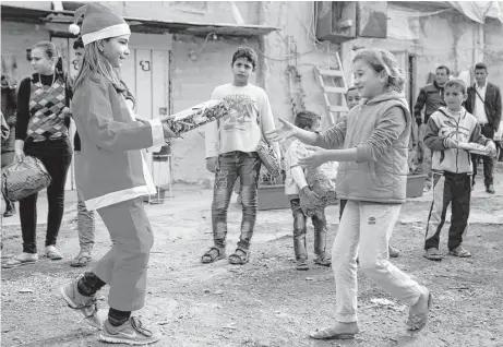  ?? Patrick Baz / AFP / Getty Images ?? Chloe, a Lebanese Christian teenager dressed as Santa Claus, hands a gift to a Syrian refugee during a gift distributi­on organized by the Maronite congregati­on Mission de Vie in a slum in the town of Dbayeh, north of Beirut.