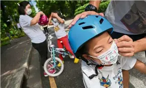  ?? — aFP ?? Safety first: a man putting on his son’s mask as his wife and daughter put on helmets at lumpini Park in Bangkok. It was their first trip outside after a three-week home quarantine due to Covid-19 fears.