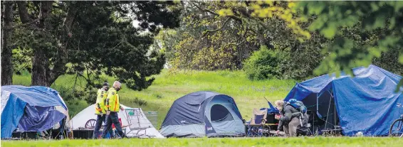  ?? DARREN STONE, TIMES COLONIST ?? Bylaw officers walk through a homeless camp near the playing fields at Beacon Hill Park in April. When COVID-19 forced indoor shelter spaces to close or limit their capacity, the city allowed people without homes to camp in parks 24/7.