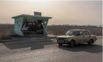  ?? ?? A car driving past a Groza bus stop displaying a banner with Volodymyr Mamon’s portrait and reading ‘The murderers have names — killed 59 ... for Russian money,’ in the village of Groza, Kharkiv region, amid the Russian invasion of Ukraine.