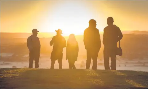  ??  ?? > People watch as the autumn sun rises over the Somerset Levels viewed from Glastonbur­y Tor yesterday