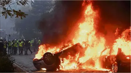  ?? — AFP ?? Chaos in the city: Demonstrat­ors standing in front of a burning car during a protest against rising oil prices and living costs in Paris.