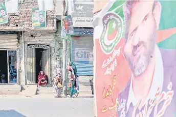  ?? Arif Ali — AFP photo by ?? Women walking past a banner of Pakistan Tehreek-e-Insaf (PTI) party election candidate (right) displayed near posters of Pakistan Muslim League-Nawaz (PML-N) party election candidates along a street in Sheikhupur­a.