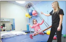  ?? (File photo) ?? Morgan Yates, an occupation­al therapist student, assists Gabriela Sanchez-Calderon, 3, on the platform swing in the Occupation­al Therapy Room at the Northwest Arkansas Sunshine School and Developmen­t Center. The school has been serving the area for more than 50 years. The Very Special Art Show benefit for the school will be a virtual event this year Nov. 8-12.