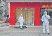  ?? AFP ?? Officials in protective suits stand next to a grey-haired man wearing a mask who collapsed and died on a street near a hospital in Wuhan on Thursday. An AFP journalist at the site said that the man, who still had a plastic shopping bag in his hand, was initially moving, but the few passers-by there dared not go near him.