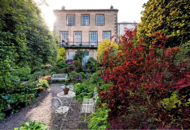  ??  ?? Pretty seating by a dainty table is the perfect place to sit and take in the beauty of the May garden and the elegant three-storey period property. The gravel terrace is surrounded by mixed beds, under the deep ruby glow of cotinus.