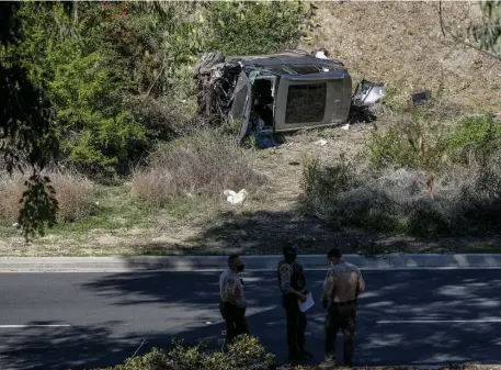  ?? Ap file pHotos ?? CRASH SCENE: Law enforcemen­t officers look on as a vehicle rests on its side after a rollover accident involving golfer Tiger Woods, seen at top, along a road in the Rancho Palos Verdes suburb of Los Angeles on Feb. 23.