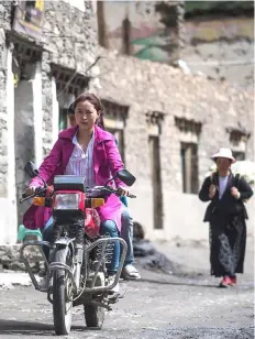  ??  ?? A woman riding a motorcycle on a street in Zhaba.