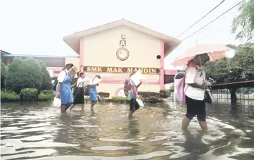  ??  ?? Students of Sekolah Menengah Kebangsaan Mak Mandin walk through the flood at their school in Butterwort­h after flash floods in that area. — Bernama photo