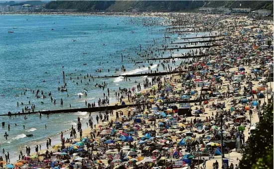  ?? Glyn Kirk - 25.jun.20/AFP ?? Banhistas aproveitam onda de calor na praia em Bornemouth, no litoral do sul do Reino Unido, país europeu mais afetado pelo vírus