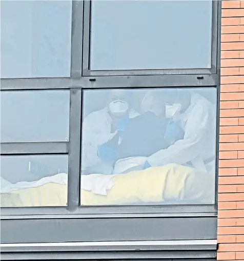  ??  ?? Two care workers wearing protective suits are seen through a window inside the Monte Hermoso retirement home in Madrid, where 20 residents died last week