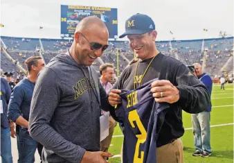  ?? Tony Ding / Associated Press ?? Former Yankees shortstop Derek Jeter (left), who grew up in Kalamazoo, receives a Michigan jersey from head coach Jim Harbaugh before the Wolverines’ 31-0 win over BYU in Ann Arbor.