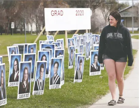  ?? JIM WELLS ?? Grade 12 student Emily Penzo walks by grad photos outside Foothills Composite High School in Okotoks. A committee at the school hatched a plan to have the school’s multiple grad photos enlarged and put on the front lawn. The feedback and response have been incredibly emotional and satisfying, says Grade 12 vice-principal Derek Markides.