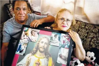  ?? AP PHOTO/RAMON ESPINOSA ?? Maria Gonzalez Munoz, right, and Juan Manuel Gonzalez pose with an image of Jesus surrounded by photos of her sister, Ramona, when she was sick and during her funeral, in San Juan, Puerto Rico.