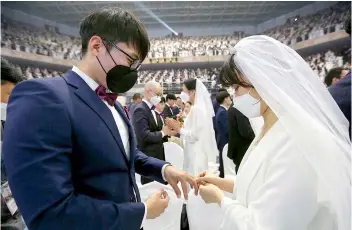  ?? —AP ?? A couple wearing face masks exchanges their rings in a mass wedding ceremony at the Cheong Gapyeong: Shim Peace World Centre in Gapyeong, South Korea, on Friday. South Korean and foreign couples exchanged or reaffirmed marriage vows in the Unificatio­n Church’s mass wedding arranged by Hak Ja Han Moon, wife of the late Rev. Sun Myung Moon, the controvers­ial founder of the church.