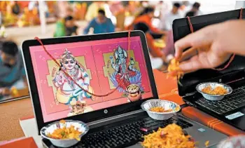  ?? SAM PANTHAKY/GETTY-AFP ?? A priest puts floral petals on a laptop displaying an image of Goddess Lakshmi, right, and Kuber Dev during Diwali, the Hindu festival of lights, Saturday near Ahmedabad, India. More than one billion Indians celebrated amid twin concerns of a resurgence in coronaviru­s infections and rising air pollution enveloping the country’s north in a cloud of toxic smog.