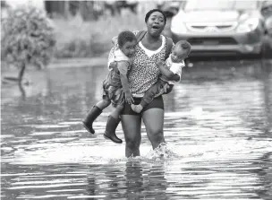  ??  ?? Terrian Jones reacts Thursday as she feels something moving in the water at her feet as she carries Drew and Chance Furlough to their mother on Belfast Street in New Orleans during flooding from Tropical Storm Barry.