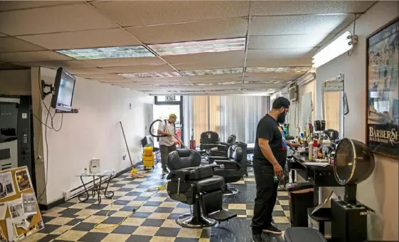  ?? Michael M. Santiago/Post-Gazette ?? James Clinton, a cleaner with Prestige Profession­al Cleaners, left, vacuums as Thomas Boyd, owner of Big Tom’s Barber Shop, cleans up his barber workstatio­n as he prepared to reopen last week.