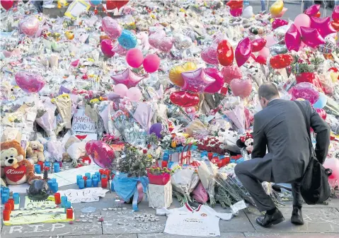  ?? REUTERS ?? A man crouches in front of flowers, messages and tokens left in tribute yesterday to the victims of Monday’s Manchester Arena attack.