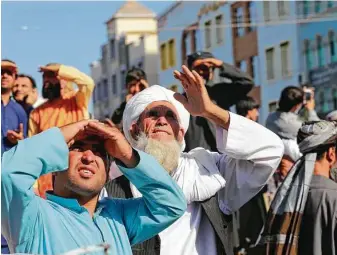  ?? Associated Press ?? People look up at a dead body hanged from a crane Saturday in the main square of Herat in western Afghanista­n. A witness said the bodies of four men were brought to the main square.