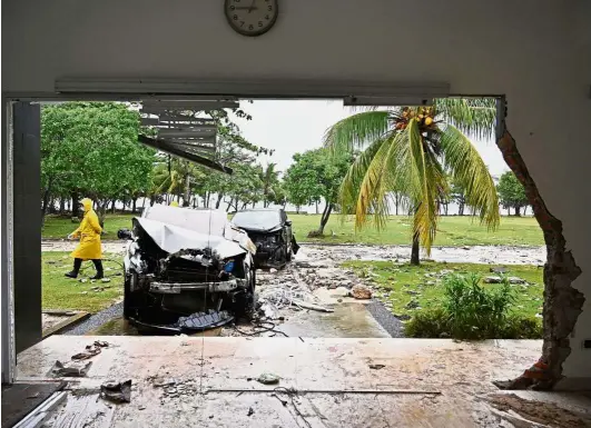  ??  ?? Heavy damage:A security officer walking past cars damaged by the tsunami at the Tanjung Lesung Beach resort in Banten province. — AFP