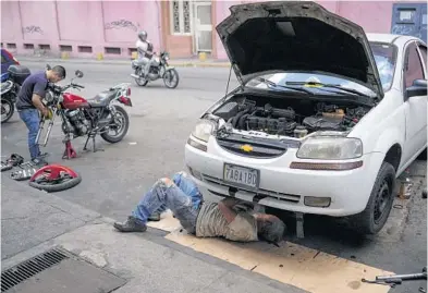  ?? MATIAS DELACROIX/AP ?? Carlos Valero repairs his car’s exhaust system last month in the San Agustin neighborho­od of Caracas, Venezuela.