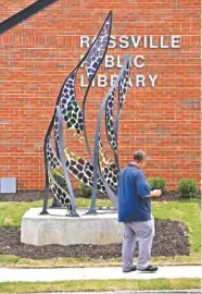  ?? STAFF PHOTO BY ROBIN RUDD ?? A passerby considers a yet-unnamed metal and glass mosaic sculpture by Chuck Peters of Cloudland, Ga., which graces the lawn of the newly renovated Rossville Public Library on Wednesday in Rossville.