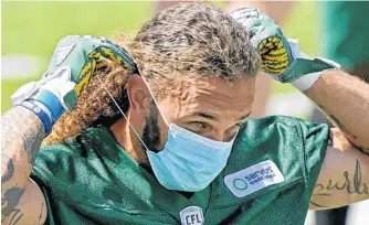  ?? POSTMEDIA NEWS ?? Edmonton Elks defensive halfback Aaron Grymes puts on a face mask during training camp at Commonweal­th Stadium in Edmonton on July 12. The Canadian Football League team has had 12 players test positive for COVID-19 since Sunday and their scheduled game against the Toronto Argonauts on Thursday was postponed.