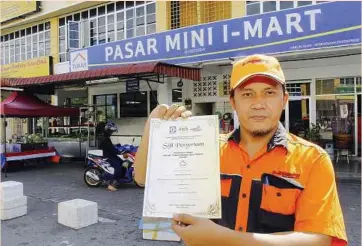  ??  ?? No mean feat: Karim showing the certificat­e of attendance for the Tukar Programme in front of his shop in Kepala Batas. The engineer-turned-entreprene­ur believes strongly that there is a future for small traders in the country.
