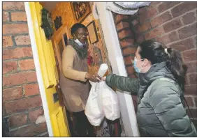  ??  ?? Volunteer Maria Martinez (right) hands bags of West Indian meals to Bridgette Toussaint prepared by members of the Preston Windrush Covid Response team in Preston, England.