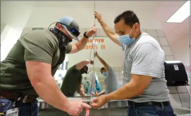  ?? (AP/LM Otero) ?? Matt Attaway (left) and Rogelio Ponciano of the Richardson Independen­t School District in Dallas install a plexiglass barrier Wednesday on a sink in a student restroom at Bukhair Elementary School.