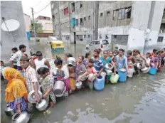  ?? — Reuters ?? People queue to collect drinking water from a municipal tanker at a flooded residentia­l colony in Ahmedabad on Saturday.