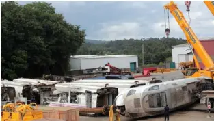  ??  ?? A MEMBER of the Spanish National Police stands next to train wreckage at a warehouse in Escravitud­e, 20 km. from Santiago de Compostela, yesterday.