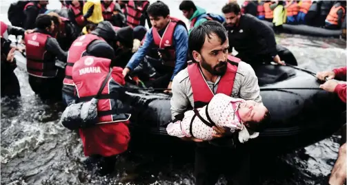  ??  ?? LESBOS: A migrant carries his baby as they come ashore along with other refugees and migrants arriving on the Greek Island of Lesbos after crossing the Aegean Sea from Turkey. — AFP