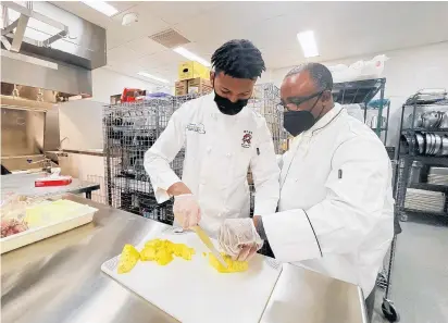  ?? CAROLE SHARWARKO/DAILY SOUTHTOWN PHOTOS ?? Chef Mark Crawford helps junior Malachi Baines with his knife skills during a culinary class at Rich Township Fine Arts and Communicat­ions Academy.