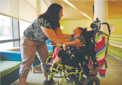  ?? Andy Cross, The Denver Post ?? Jennifer Fischer adjusts her daughter Cecilia’s position in her wheelchair between appointmen­ts at Children’s Hospital Colorado in Aurora last month. Cecilia, 9, suffered a brain injury when she was 11 months old. She requires around-theclock attention from her family, which relies on Medicaid as a secondary insurer.