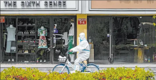  ?? Andy Wong The Associated Press ?? A worker rides a bicycle past shuttered shops after authoritie­s ordered the closing down of businesses Monday in Beijing.