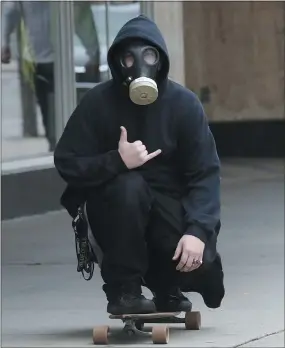  ?? DAVE SCHERBENCO - ASSOCIATED PRESS ?? A skateboard­er makes the “Hang Loose” sign Tuesday as he rolls a sidewalk in WilkesBarr­e, Pa., while wearing a gas mask.