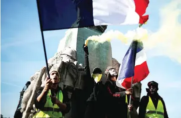  ??  ?? Protesters wearing yellow vests hold French flags and a safety flare during a demonstrat­ion by the ‘yellow vests’ movement in Paris. — Reuters photo